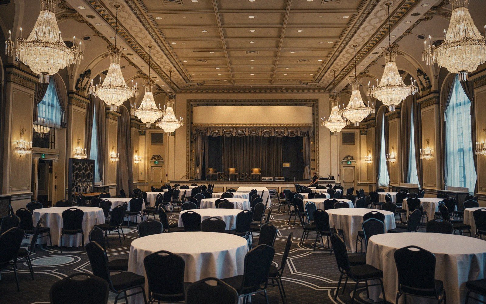 Large hotel ballroom with banquet tables set and house lights on, no event in progress