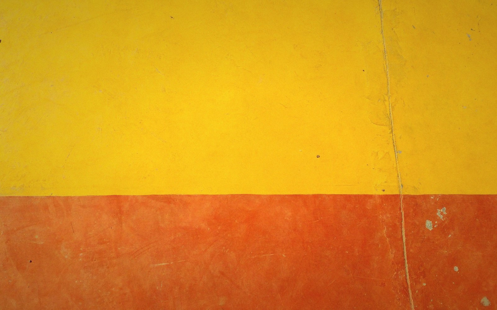 Weathered wall painted in yellow and orange bands, with a vertical crack running through both